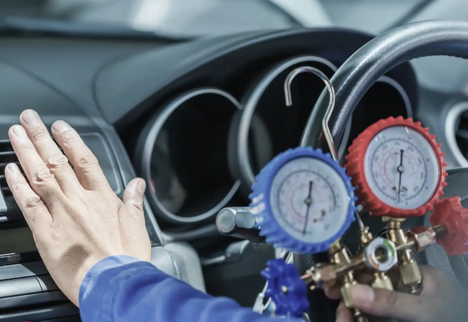 Auto air conditioning repair and refrigerant recharge shown by A technician checks a car’s air conditioning system using pressure gauges, placing one hand near the air vents inside the vehicle.