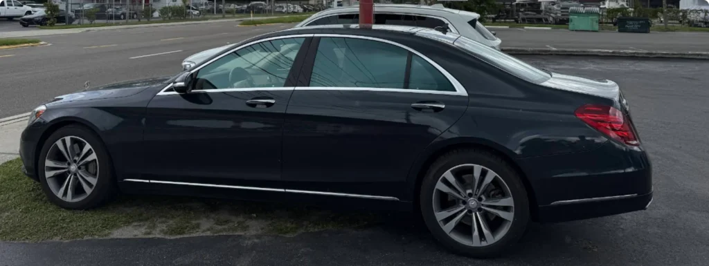 A black Mercedes- Benz sedan is parked on a grassy patch next to a road, with another car visible in the background.