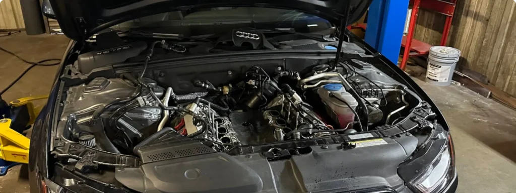 A VW car with its hood open in a garage, showing a partially disassembled engine and exposed components, surrounded by tools and equipment. in My Car Guy auto repair Plant City FL.