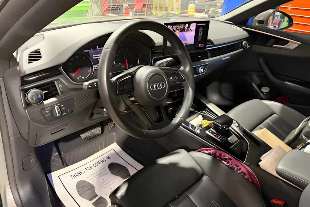 Interior of an Audi vehicle showing the steering wheel, dashboard, and center console with the infotainment screen turned on.