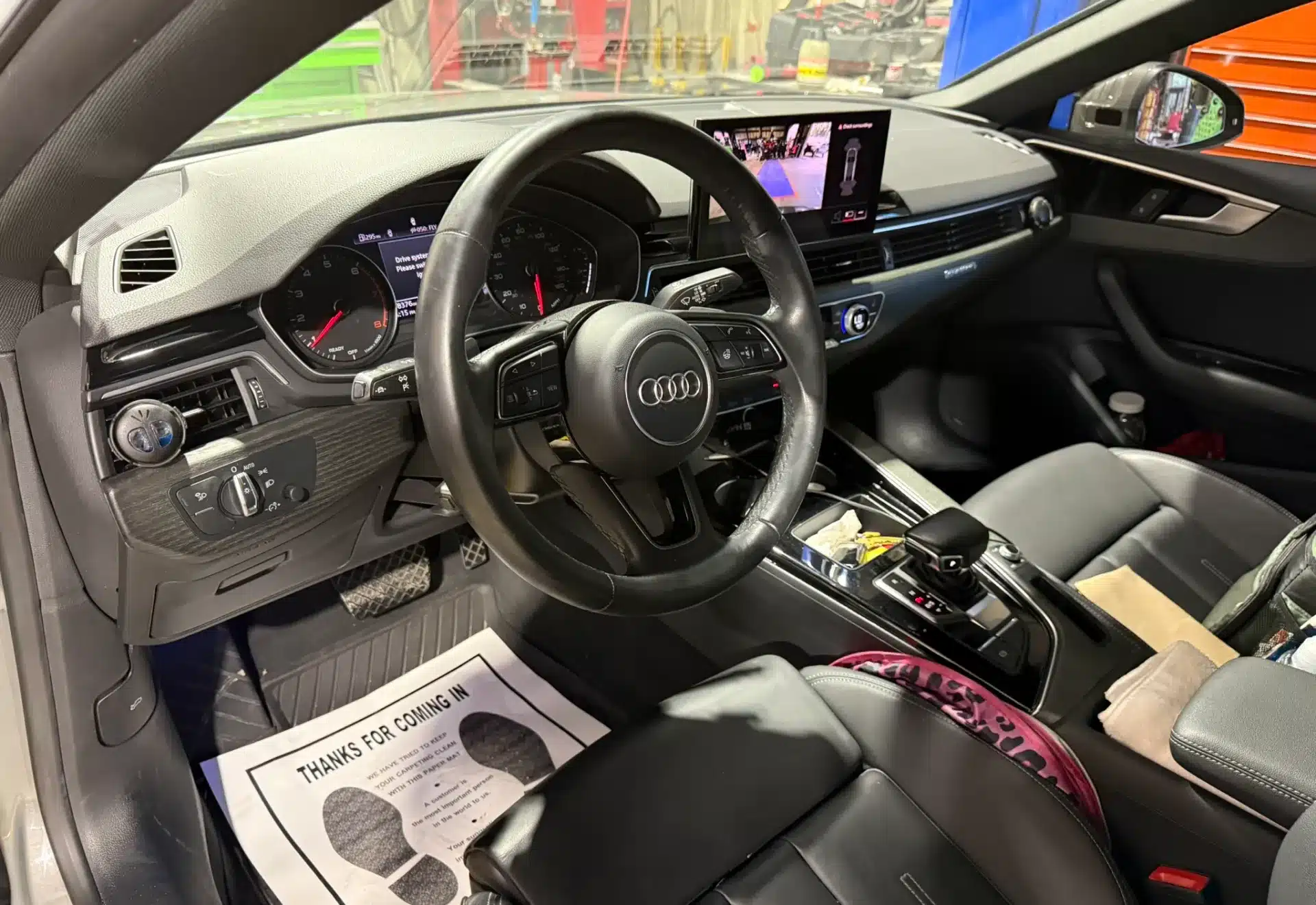 Interior view of a luxury car featuring a sleek dashboard, leather steering wheel with an Audi logo, digital display, and leather seats. The atmosphere is modern and sophisticated.