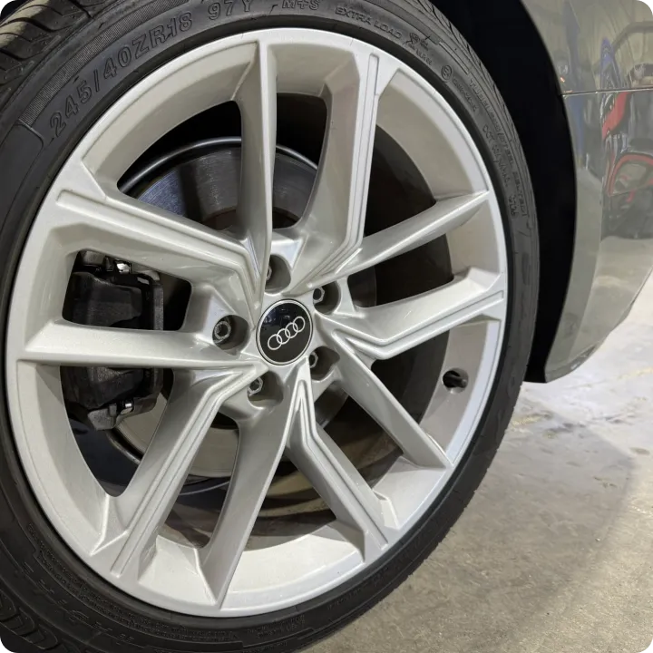 Close-up of a silver Audi car wheel showcasing the intricate, sleek alloy spokes and the brand logo at the center, parked on a concrete floor.