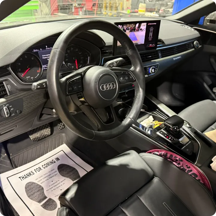 Interior view of a luxury car featuring a sleek dashboard, leather steering wheel with an Audi logo, digital display, and leather seats. The atmosphere is modern and sophisticated.
