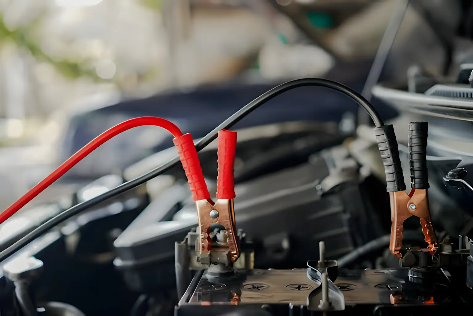 Close-up of a car battery with red and black jumper cables attached. The scene conveys a sense of repair and readiness, highlighting the auto repair context.